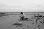 Here's a short alt tag for the image: `Person writing on beach, black and white.`